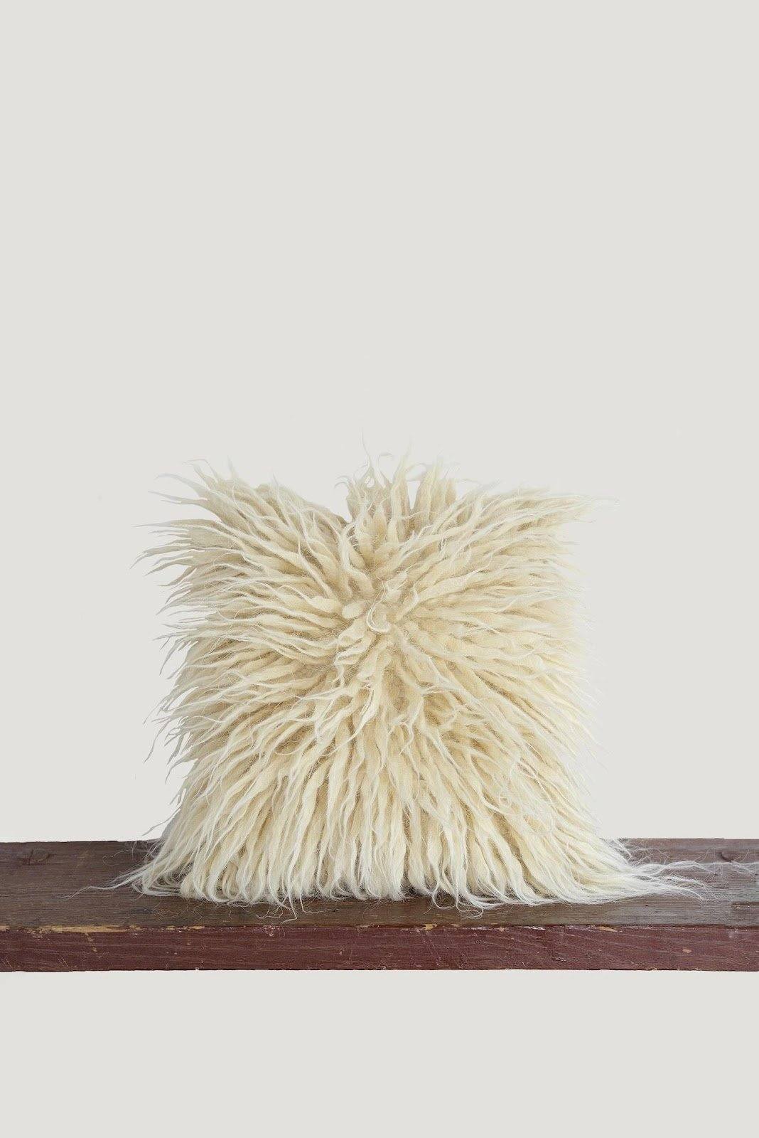 Fluffy white wool pillow, natural fibers, resting on brown wooden surface against plain backdrop