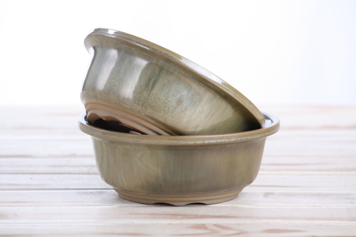 Two rounded ceramic pots with a green glaze on a light wooden surface