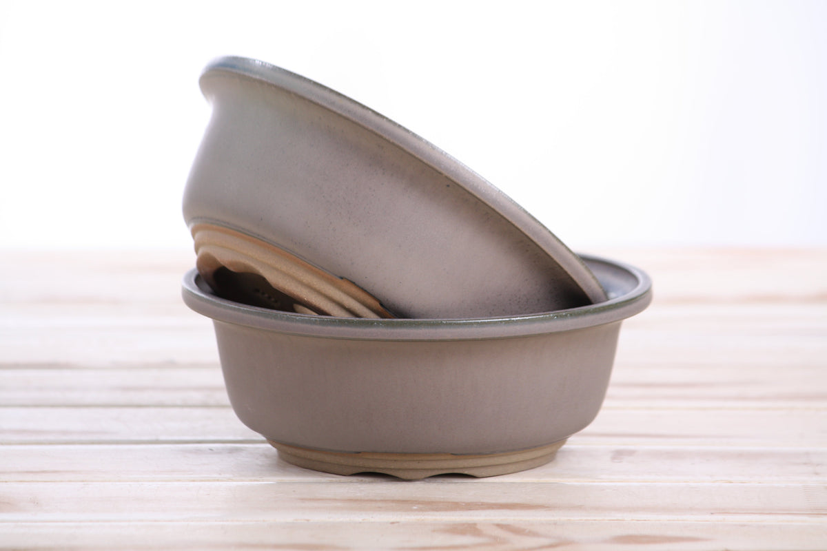 Two stacked ceramic bonsai pots with a speckled green rim on a wooden surface.