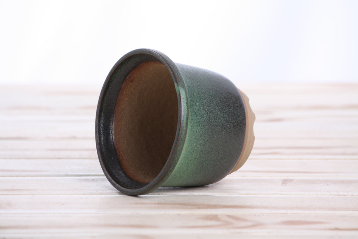 Green ceramic bonsai pot with slightly ridged rim, earth-toned interior, placed on a light wooden surface.