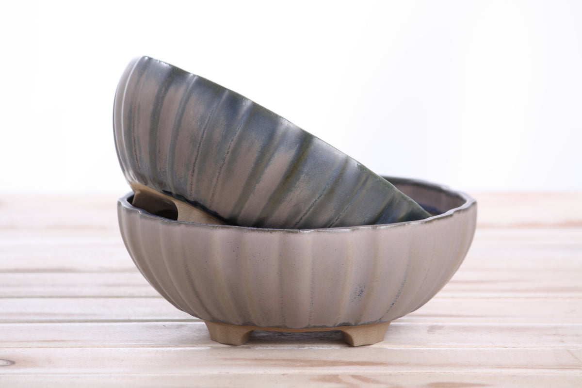 Two handmade ceramic pots with a ribbed design on a wooden surface.