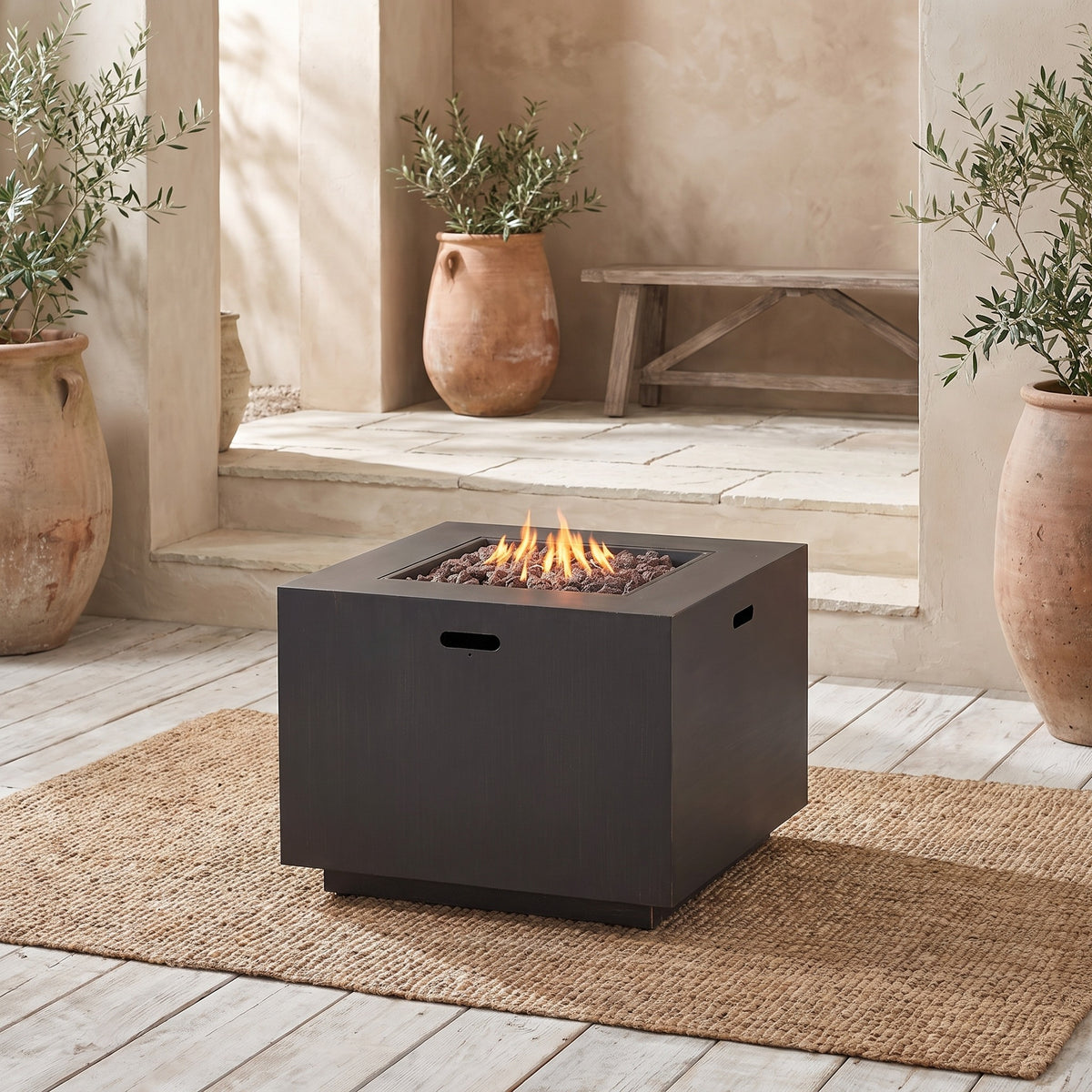 A 33" outdoor iron square propane fire pit with a brushed brown finish, lit with flames, placed on a woven mat in a rustic outdoor setting with terracotta pots and plants。