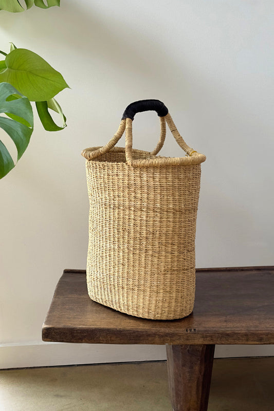 Woven basket with single handle placed on wooden table with green leaf in background