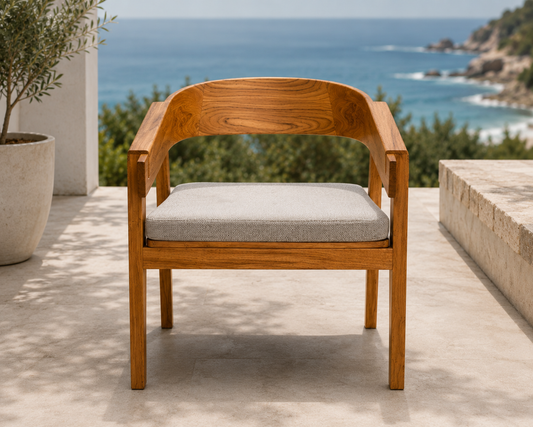 Teak round back arm chair with cushion on patio, ocean and cliffs in the background