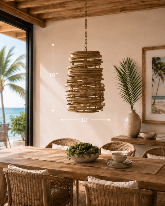 A natural woven pendant lamp with dimensions 19" H x 12" diameter, hanging above a dining table in a sunlit room with a view of palm trees and ocean.