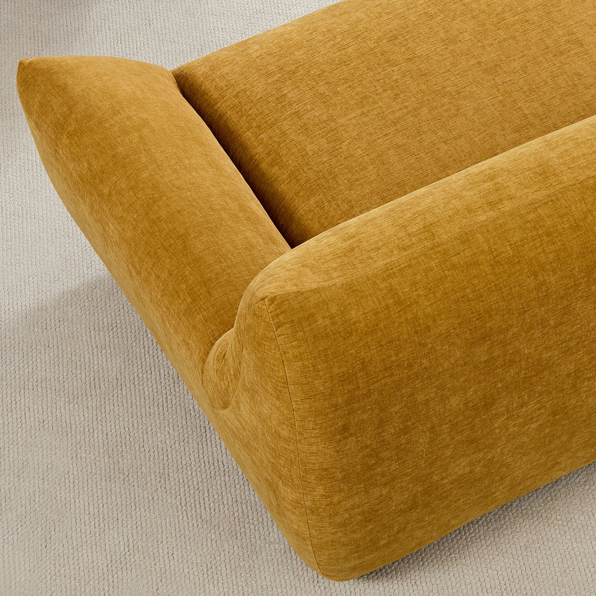 A mustard-colored sofa corner with textured fabric on a cream rug