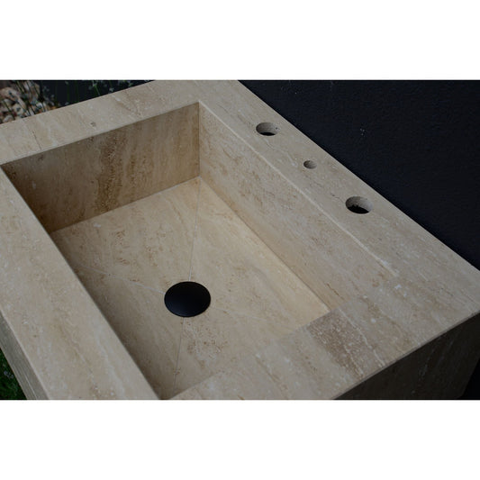 Rectangular travertine sink with a black drain and faucet holes.