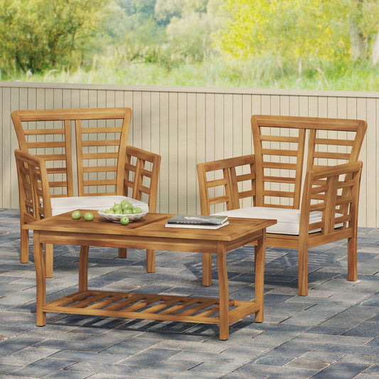 Twin teak wood chairs and square table with a bowl of green apples and a book on the table, placed on a stone patio with a wooden fence backdrop.