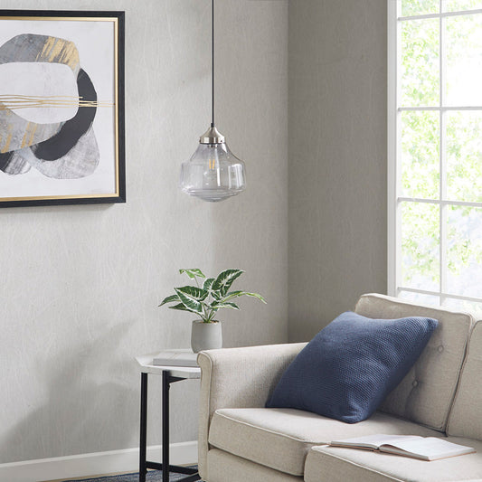 Smoke-grey bell-shaped glass pendant light with antique brass ceiling mount, hanging over a beige sofa with a blue pillow, next to a small table with a plant and a print on the wall.