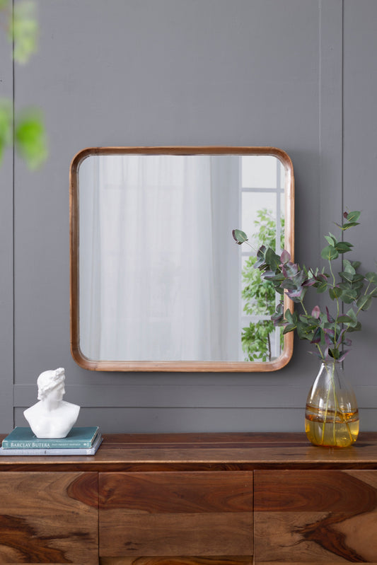 32"x32" square mirror with wood frame on wooden console, greenery and bust, grey wall.