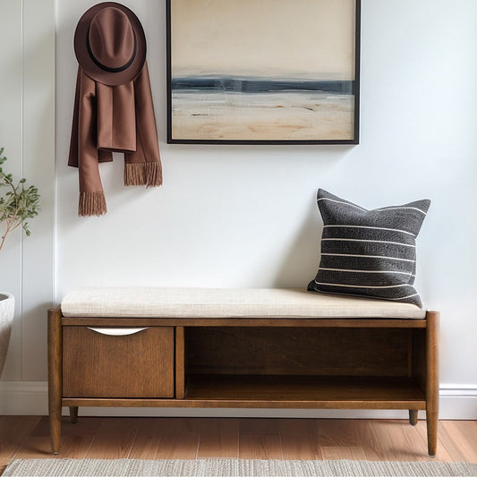 Wooden bench with storage drawers and upholstered cushion, brown hat and scarf hanging on wall, cushion with striped pattern.