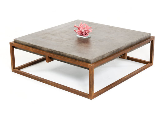 A square concrete and metal coffee table with a pink coral decoration on it.