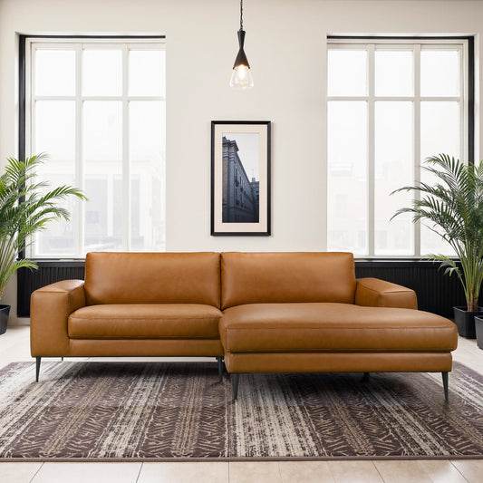 Light brown leather sofa with modern design, thin legged on patterned rug, black frames and windows, hanging light, indoor plants, art piece on wall.
