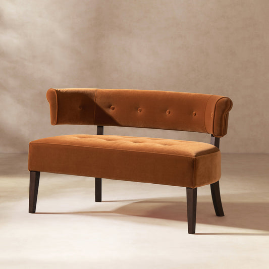 A tufted bench settee with a burnt orange velvet upholstery and dark wood accents.