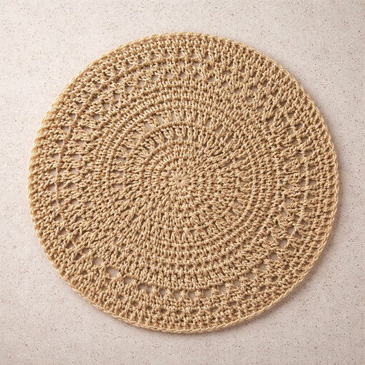 Circular woven placemat with intricate pattern in tan on marble background