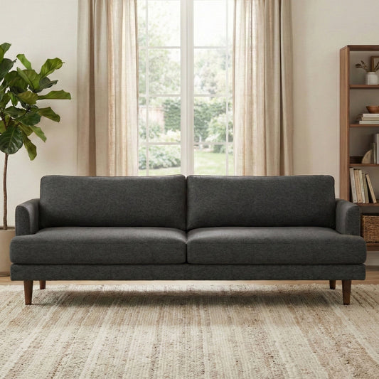 Dark grey sofa with simple design, light tan carpet, windows with curtains, indoor view