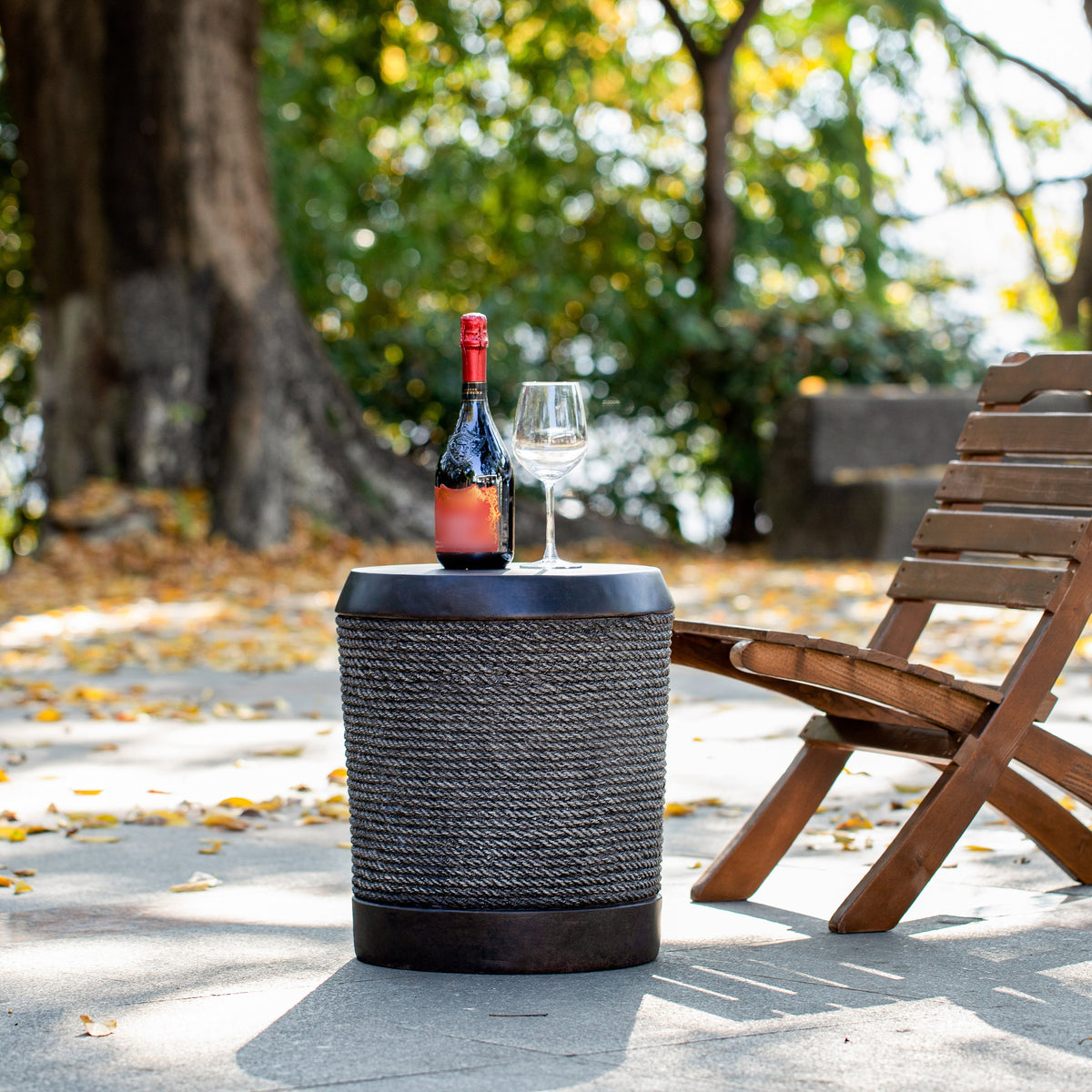 Outdoor dark brown table with rope finish and vintage trim holding wine bottle and glass in autumnal setting