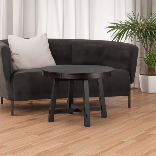 A grey upholstered sofa with a round extensible dining table in front, a wooden floor, neutral curtains, and a potted plant in the corner.