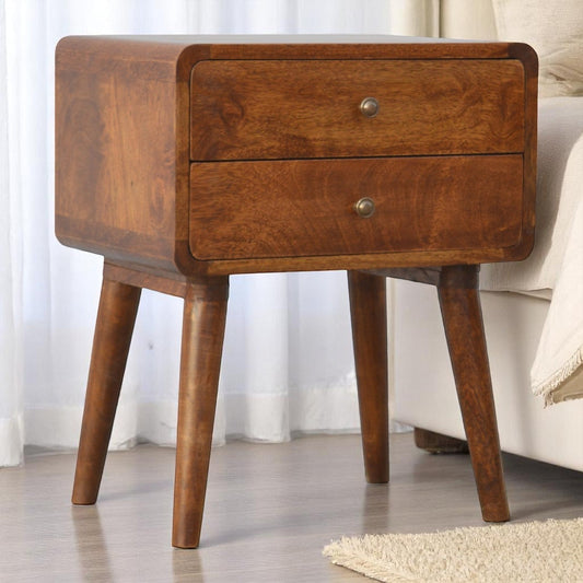 Small, medium-toned wood nightstand with curved top and two drawers, placed beside a couch in a softly lit room.