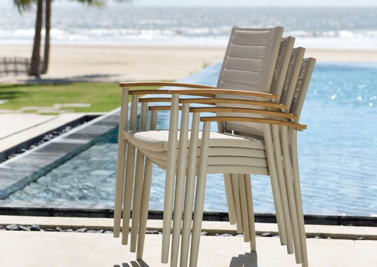 Stacked armchairs with wooden legs and woven seats by a pool overlooking the beach.