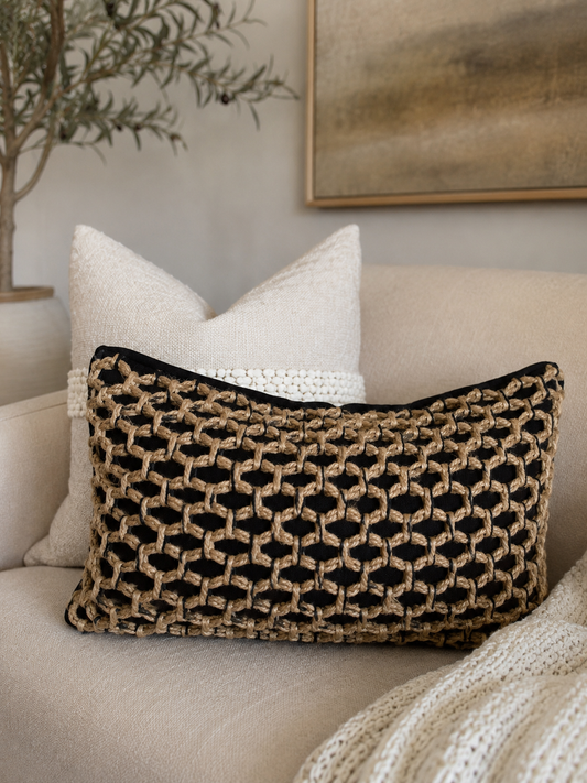 Woven basket-like lumbar pillow cover in tan and black, placed on beige sofa