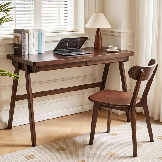 Dark brown wooden desk with laptop and chair, books, and lamp on wooden floor with rug, neutral wall, window blinds.