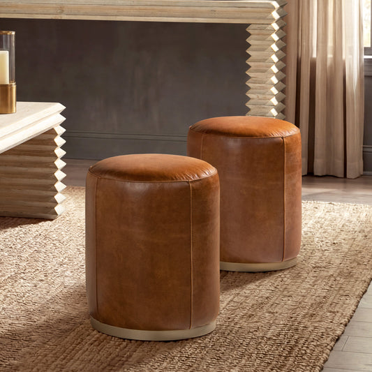Two round leather ottomans on a textured rug, camel brown, against a wooden mirror and candle