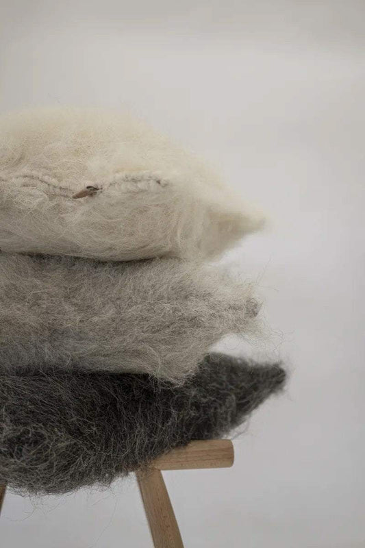 Stack of organic wool pillows on wood stand, muted colors.