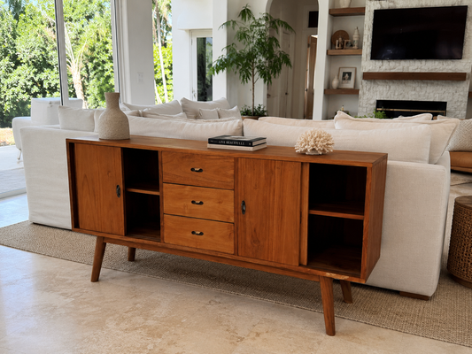 Dark teak wood buffet with drawers and open shelves, placed next to a light beige sofa