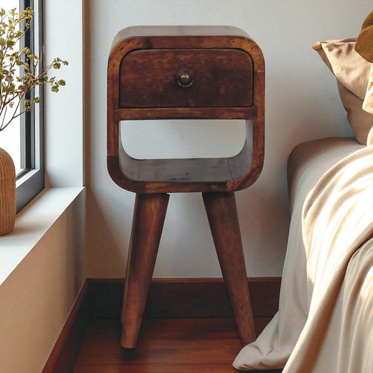 Vintage wood nightstand with single drawer, standing against a wall with sunlight from a nearby window, beside beige bedding.