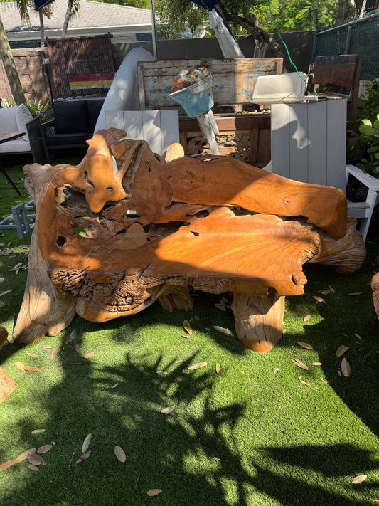 Large, organic-shaped sofa made from teak wood with natural knots and grain on a grassy yard.