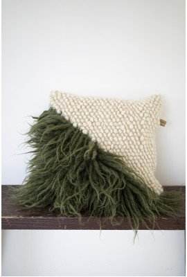 Handwoven pillow with natural fringes and a diamond pattern, predominantly white with green accent, placed on a ledge.