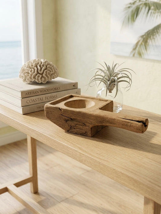 Wooden planter with handle on a table, small glass with air plant, books and coral decoration, beach window view in the background.
