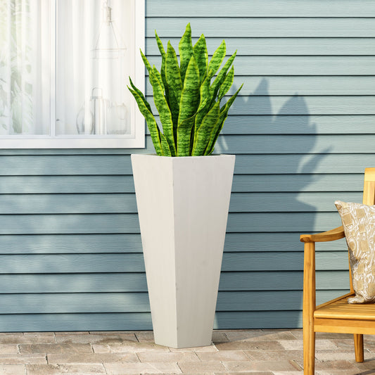 A tall white garden planter with a snake plant on a patio next to a wooden bench with a cushion and a house facade in the background.