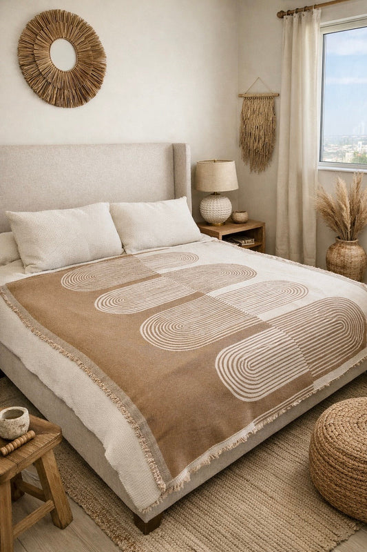 Beige and brown throw blanket with geometric pattern on neatly made bed, beige walls, circular rug detail, wooden stool, woven pouf, natural decor elements