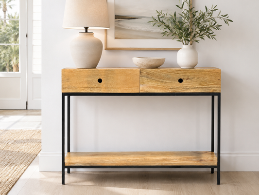 A rustic wooden console table with two drawers, black metal frame, lamp, bowl, vase, and framed picture in a minimalist room.