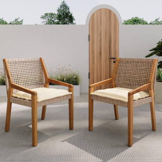 Two outdoor dining chairs with acacia wood frames and wicker seats with cream cushions, placed on a patio with a wooden door in the background.