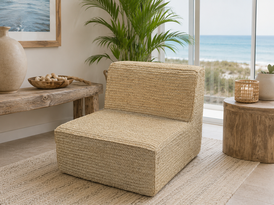 A handwoven lounge chair made from natural materials, placed on a neutral-toned rug in a room with ocean views through a modern window.
