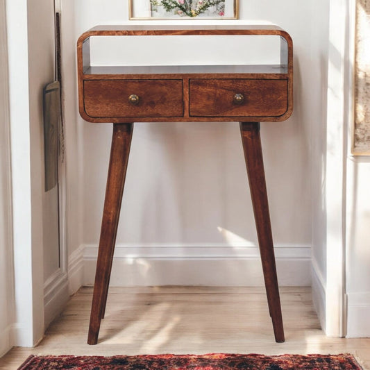 A solid wood mini curved honey console table with two drawers, placed against a white wall in a minimalist room setting.