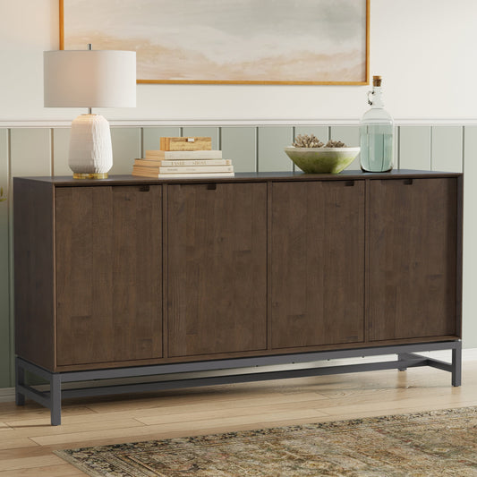 Solid wood buffet with four doors, placed against a wall with a lamp and book on top; light wood floor and green panel backdrop, framed artwork above.