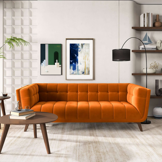 A burnt-orange mid-century modern velvet sofa with a tufted design in a room with geometric elements and abstract paintings on the wall.