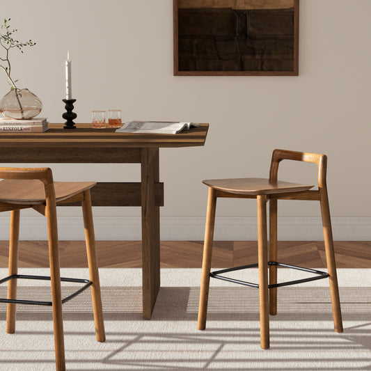 A modern minimalist low back wood counter stool with a backrest and metal support frame in a dining room setting with a wooden table and decorative items.