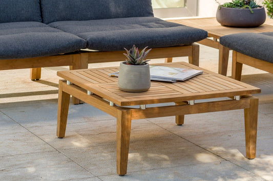 Teak Arno Square Side Table with silver accents, grey plant and book, blue sofa backdrop, outdoor setting