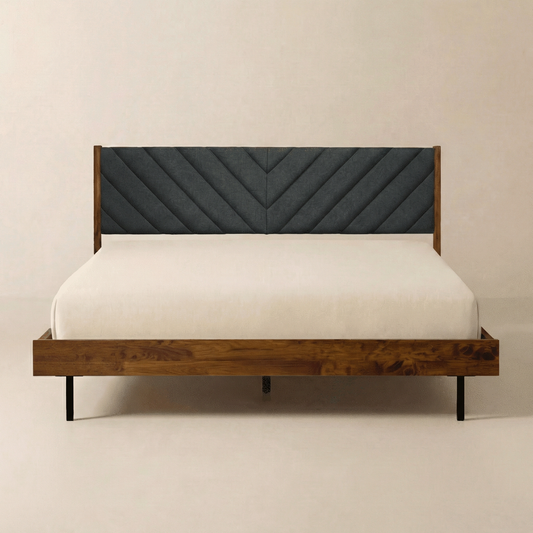 A wooden bed frame with a gray upholstered headboard, white bedding, and simple black legs against a plain wall.