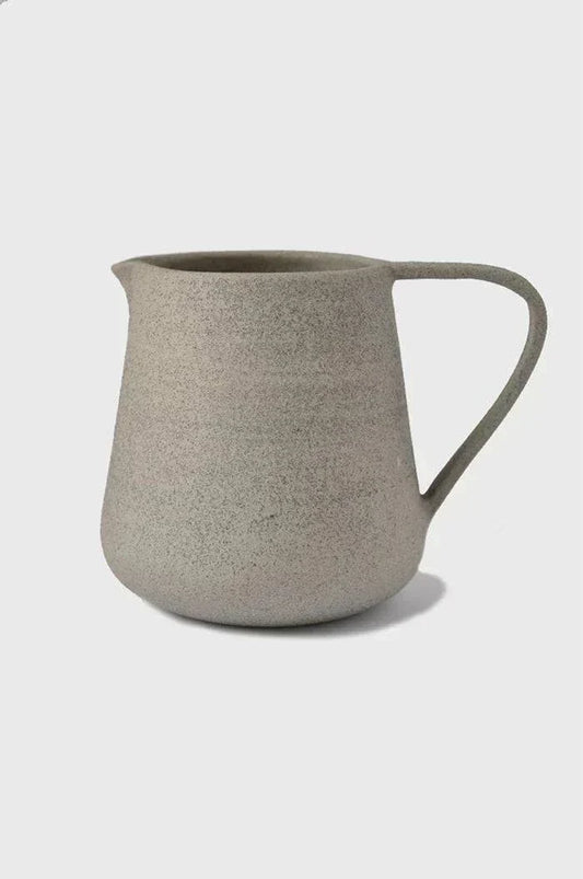 Textured ceramic pitcher with a single handle against a plain background.