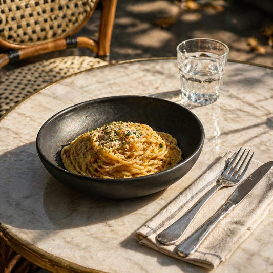 Black matte stoneware pasta bowl with spaghetti on a marble table, outdoor setting