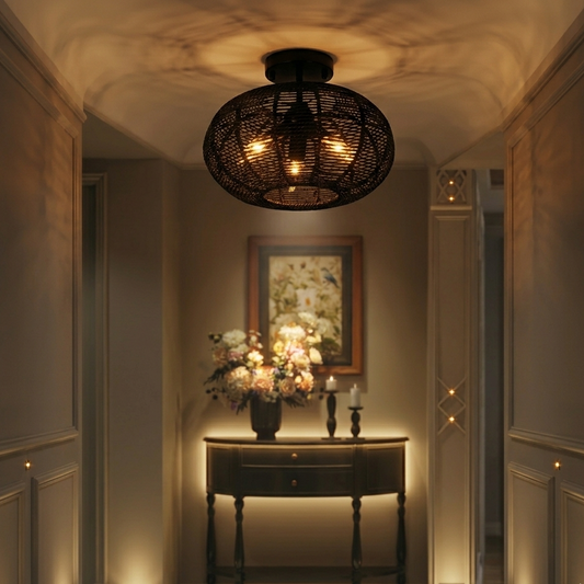 Oval rattan light fixture in dark finish mounted on a ceiling, illuminating a hallway with a table, flowers, and candles below.