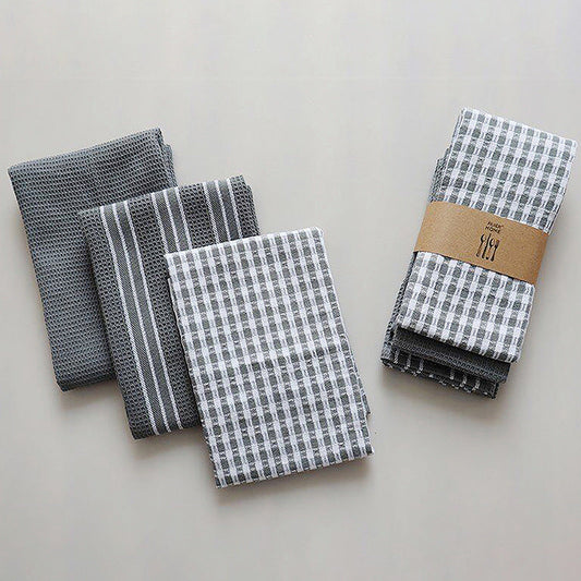 Three sets of woven kitchen towels with various patterns (stripes, checks) on a light background, bound with a brown band, likely displaying a brand logo.