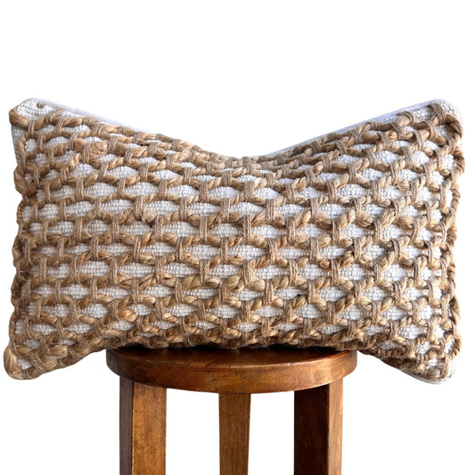 A woven lumbar pillow cover with a basketweave pattern, featuring a beige and white color scheme, displayed on a wooden stool against a plain background.