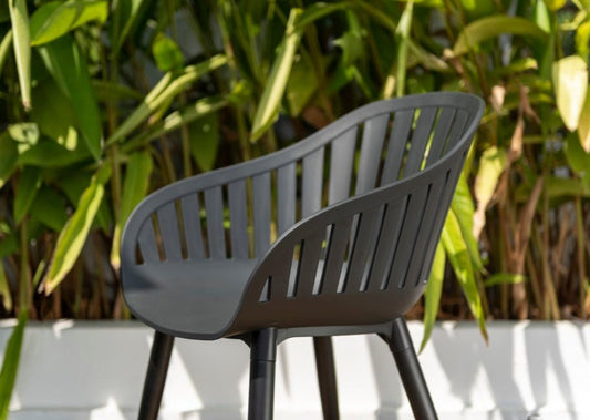 Modern dark grey slatted resin chair with metal legs, placed outdoors with green foliage in the background